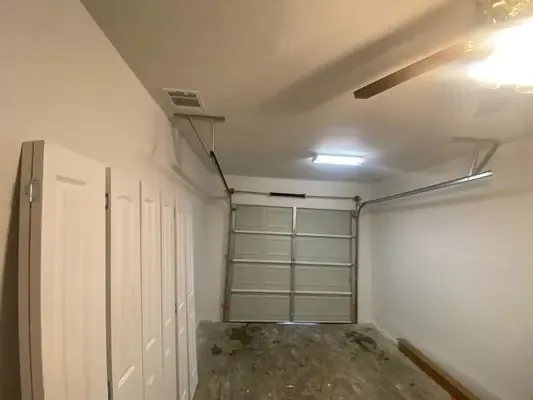 Interior view of a residential garage mid-repair, opener rail and ceiling framing visible